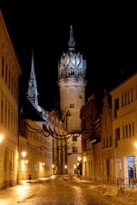 Naktinis istorinės gatvės vaizdas su ap&scaron;viestu bok&scaron;tu ir pensiono "Zur Elbe" pastatais ramioje kaimynystėje.