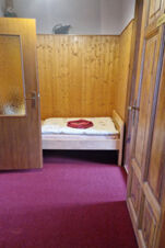 Nedidelis, paprastai įrengtas kambarys su medinėmis sienomis, raudonu kilimu ir lova pensione "Zur Elbe".