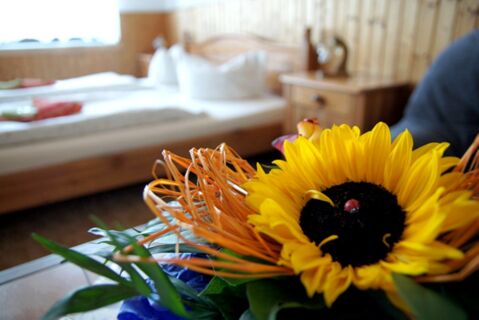 Vaizdas į jaukų pensiono "Zur Elbe" kambarį su medinėmis lovomis ir dekoratyvine saulėgrąžų puok&scaron;te pirmame plane.