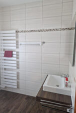 Modernus ir &scaron;varus pensiono "Zur Elbe" vonios kambarys su baltu radiatoriumi, stačiakampiu praustuvu ir mediniu stalvir&scaron;iu.