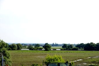 Platus, žalias kra&scaron;tovaizdis su medžiais ir vandens telkiniais, vaizdas i&scaron; pensiono Zur Elbe į ramų Elbės slėnį po giedru dangumi.