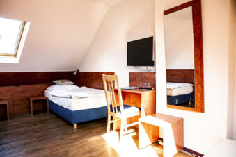 Hell eingerichtetes Einzelzimmer mit Holzfu&szlig;boden, Schreibtisch, Fernseher und gro&szlig;em Spiegel im Hotel Haus Rheinblick.