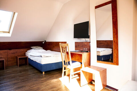 Hell eingerichtetes Einzelzimmer mit Holzfu&szlig;boden, Schreibtisch, Fernseher und gro&szlig;em Spiegel im Hotel Haus Rheinblick.