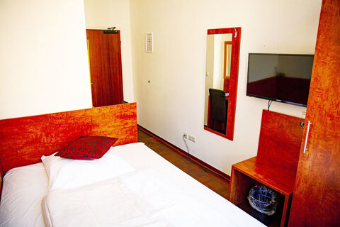 Kleines Hotelzimmer mit Holzm&ouml;beln, Bett, Spiegel und Fernseher im Hotel Haus Rheinblick in schlichtem Design.