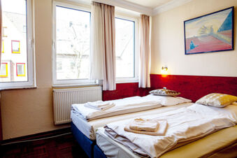 Hell eingerichtetes Hotelzimmer mit zwei Einzelbetten, Fenstern mit Vorh&auml;ngen und Kunstbild an der Wand im Hotel Haus Rheinblick.