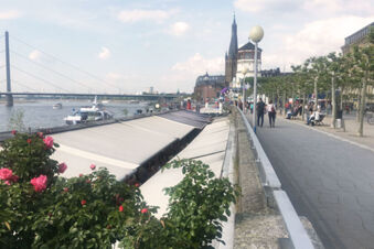 Au&szlig;enansicht der Rheinufer-Promenade mit Menschen und Blumen nahe dem Hotel Haus Rheinblick in der Altstadt.