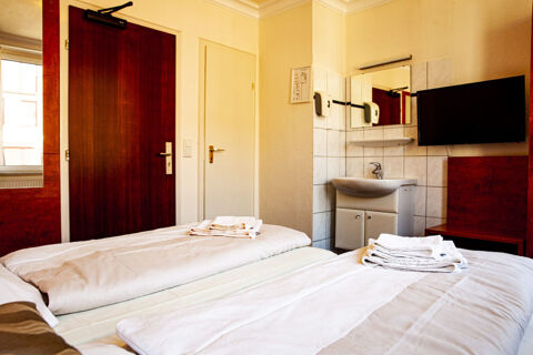 Kompaktes Hotelzimmer mit Doppelbett, Waschbecken, Fernseher und Holzt&uuml;ren im Hotel Haus Rheinblick.