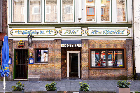 Die Fassade des Hotel Haus Rheinblick zeigt ein traditionelles Backsteingeb&auml;ude mit einem Eingangsportal und gro&szlig;en Fenstern an der Stra&szlig;e.