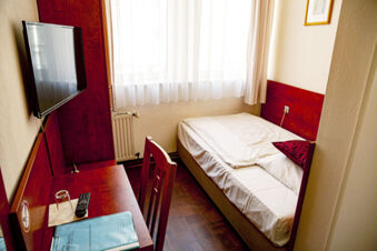Kompaktes Einzelzimmer im Hotel Haus Rheinblick mit einem Bett, Schreibtisch, Fernseher und einem Fenster mit wei&szlig;en Vorh&auml;ngen.