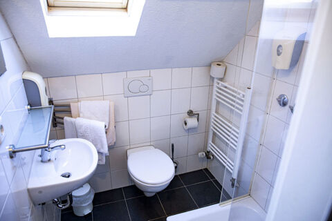 Kompaktes Badezimmer mit Toilette, Waschbecken und Dusche unter einem Dachfenster im Hotel Haus Rheinblick mit wei&szlig;en Fliesen.