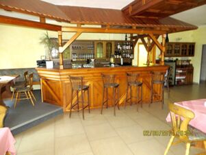 Wooden bar with five high chairs and glassware behind the counter inside Parkhotel Luckau-Cahnsdorf restaurant dining area