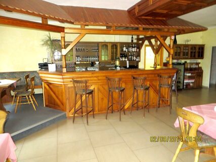 Wooden bar with five high chairs and glassware behind the counter inside Parkhotel Luckau-Cahnsdorf restaurant dining area