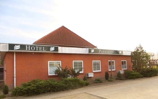 Ansicht der roten Backsteinfassade des Parkhotel Luckau-Cahnsdorf mit mehreren Fenstern und Schildern &uuml;ber dem Eingang.