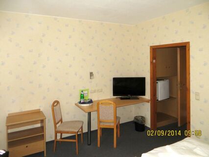 Ein einfach eingerichtetes Hotelzimmer im Parkhotel Luckau-Cahnsdorf mit zwei St&uuml;hlen, einem Fernseher auf einem Tisch und einer kleinen Minibar.