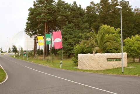 Die Au&szlig;enanlage mit Stra&szlig;enzufahrt, B&auml;umen und Fahnen zeigt den Eingangsbereich zu Tropical Islands beim Parkhotel Luckau-Cahnsdorf.
