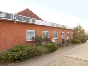 Red brick building with white-trimmed windows and signs reading Parkhotel Luckau-Cahnsdorf bordered by shrubs and a paved walkway