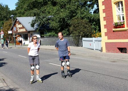 Zwei Personen mit Schutzkleidung fahren Inlineskates auf einer Stra&szlig;e vor dem Parkhotel Luckau-Cahnsdorf an einem sonnigen Tag.