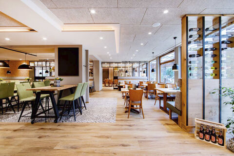 Světl&aacute; a modern&iacute; restaurace s dřevěnou podlahou, zelen&yacute;mi a hněd&yacute;mi židlemi a stojanem na v&iacute;no v Land-gut-Hotelu Heidsm&uuml;hle.