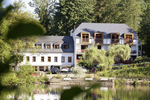 Exteri&eacute;rov&yacute; pohľad na Land-gut-Hotel Heidsm&uuml;hle s niekoľk&yacute;mi poschodiami, viditeľn&yacute;mi oknami a balk&oacute;nmi uprostred zelenej pr&iacute;rody pri jazere.