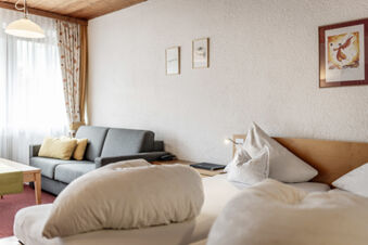 Gem&uuml;tliches Hotelzimmer im Hotel Engel mit Doppelbett, Sofa, Holzm&ouml;beln und dekorativen Bildern an der Wand.
