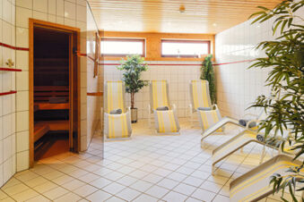 Entspannungsbereich mit Liegest&uuml;hlen, Pflanzen und Sauna im Wellnessbereich des Hotel Engel mit heller Fliesenoptik.