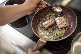 Zwei St&uuml;cke Fleisch werden in einer Pfanne mit Rosmarin und Butter im Hotel Engel auf dem Herd gebraten.