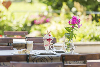 Tisch im Au&szlig;enbereich des Hotel Engel mit Kaffee, Eisbecher, Kuchen und einer Vase mit pinker Blume bei sonnigem Wetter.
