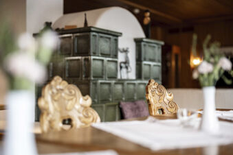 Innenansicht mit kunstvoll geschnitzten Holzst&uuml;hlen und gr&uuml;nem Kachelofen im rustikalen Stil im Hotel Engel.