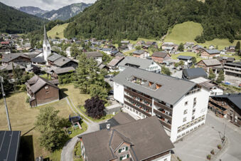 Luftaufnahme des Hotels und der umliegenden Berglandschaft mit Dorf, Kirche und Spielplatz im Hotel Engel.