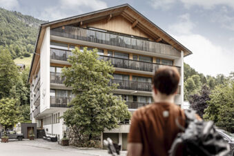 Die Fassade des Hotel Engel mit mehreren Balkonen und einem Baum im Vordergrund, die Lage in einer bergigen Landschaft ist zu sehen.