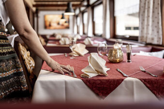Ein Tisch im Hotel Engel wird mit wei&szlig;en Servietten, Gl&auml;sern und Besteck in einem gem&uuml;tlichen Restaurant mit traditionellen Holzm&ouml;beln gedeckt.