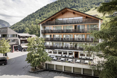 Au&szlig;enansicht des Hotel Engel mit Balkonen und Terrasse vor bewaldeten Bergen an einem bew&ouml;lkten Tag im Sommer.