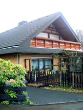 Two-story brown brick house with a large balcony and wooden fence at Fewos Privatpension Geib