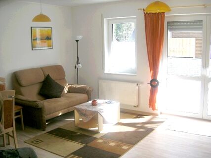Living room interior at Fewos Privatpension Geib with brown sofa, patterned rug, coffee table, orange curtain, and wall art