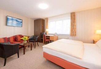 Helles Hotelzimmer im Hotel Dieck mit Doppelbett, Sitzecke, Schreibtisch und gro&szlig;em Fenster mit Vorh&auml;ngen.