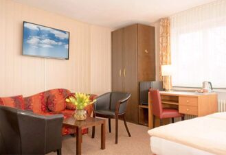 Helles und gem&uuml;tliches Hotelzimmer im Hotel Dieck mit roter Couch, zwei schwarzen Sesseln, Schreibtisch und gro&szlig;er Fensterfront.