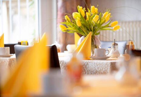 Hell gedeckter Tisch mit gelben Servietten und Tulpen als Dekoration im Restaurant des Hotel Dieck f&uuml;r einladende Mahlzeiten.