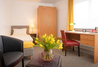 Helles Einzelzimmer im Hotel Dieck mit gelber Bettdecke, Holzschrank, Schreibtisch und einem Strau&szlig; gelber Tulpen auf dem Tisch.