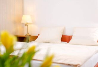 Helles und gem&uuml;tliches G&auml;stezimmer im Hotel Dieck mit gro&szlig;em Bett, beiger Bettw&auml;sche und Nachttischlampe nahe einer Holzvert&auml;felung.