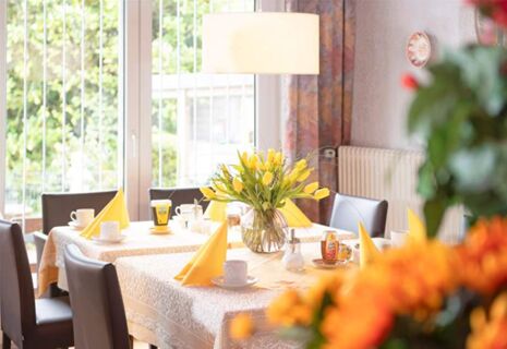 Heller und freundlich gedeckter Fr&uuml;hst&uuml;ckstisch mit gelben Tulpen im Hotel Dieck, umgeben von bequemen St&uuml;hlen am Fenster.
