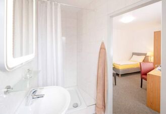 Hell gestaltetes Badezimmer mit Dusche und Waschbecken sowie angrenzendem Schlafzimmer im Hotel Dieck mit moderner Einrichtung.