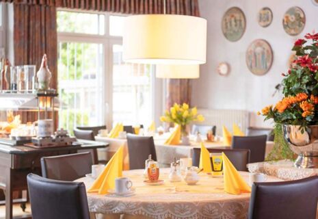 Hell und freundlich eingerichteter Fr&uuml;hst&uuml;cksraum im Hotel Dieck mit gedeckten Tischen, gelben Servietten und Blumenarrangements.