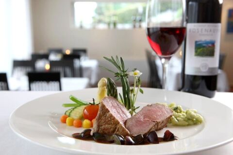 Two slices of cooked meat with sauce, vegetables, and herbs on a white plate with wine and bottle at Hotel-Restaurant Felmis Nichtraucherhaus