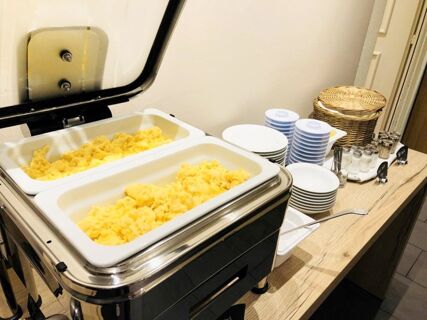 Two trays of scrambled eggs in a chafing dish next to stacks of plates, condiments, and a basket at Hotel-Restaurant Felmis Nichtraucherhaus
