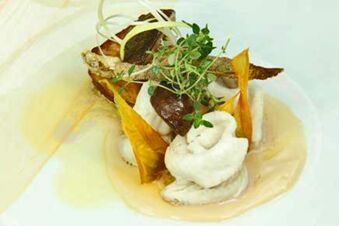 A gourmet dish with various garnishes, microgreens, and sauces presented on a white plate at Ristorante Albergo Grotto Serta