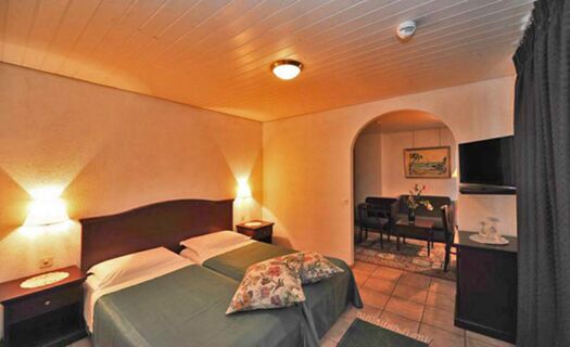 Two single beds with green covers and floral pillows in a softly lit room at Ristorante Albergo Grotto Serta with an archway leading to a sitting area