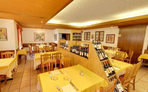 Sala de jantar acolhedora com toalhas de mesa amarelas e prateleiras de vinho no Ristorante Albergo Grotto Serta, convidativo e elegantemente mobilado.