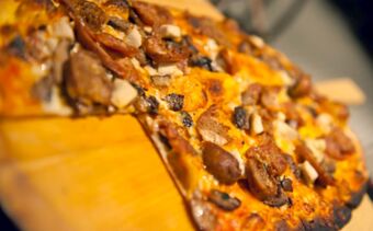 K&ouml;zelk&eacute;p egy frissen s&uuml;lt pizz&aacute;r&oacute;l gomb&aacute;val &eacute;s kolb&aacute;sszal egy fadeszk&aacute;n a Ristorante Albergo Grotto Serta &eacute;tteremben.