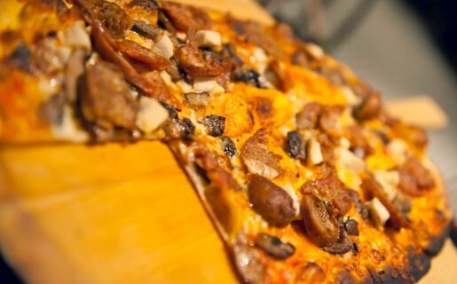 Grande plano de uma piza acabada de cozer com cogumelos e salsicha numa t&aacute;bua de madeira no Ristorante Albergo Grotto Serta.