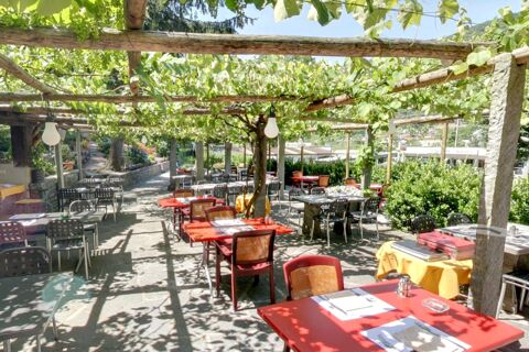 Terra&ccedil;o exterior ensolarado com mesas vermelhas e pretas sob um dossel verde no Ristorante Albergo Grotto Serta.
